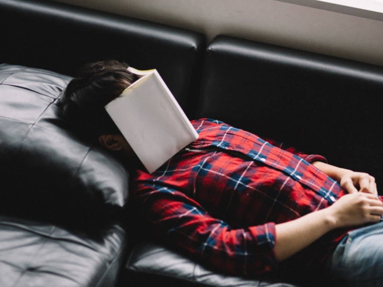 本を顔に乗せてソファーで眠る男性